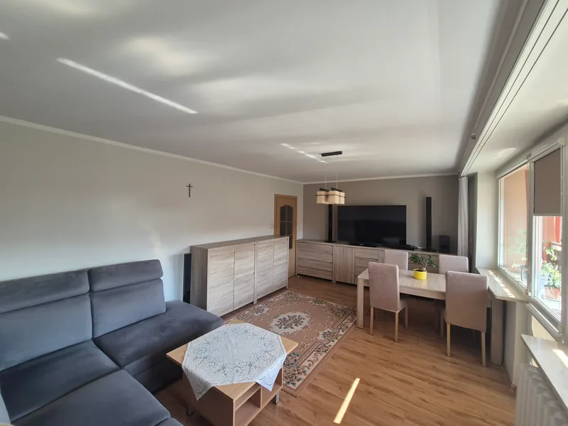 Salon z kanapą, telewizorem na komodzie i jadalnią przy oknach